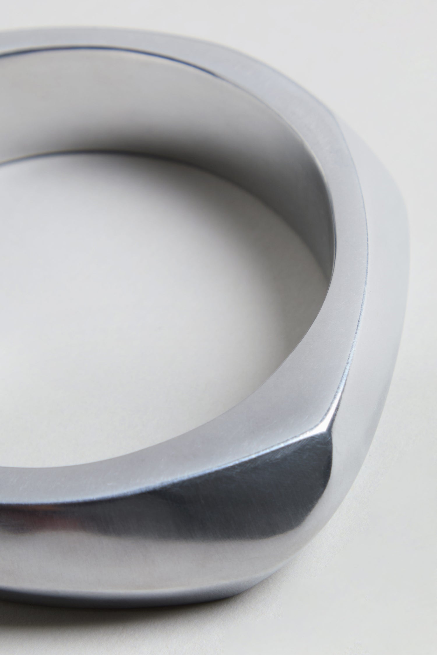 A close-up of the Statement Silver Bangle with its modern, geometric design and smooth, angular edges on a light background, capturing the essence of architectural jewelry.