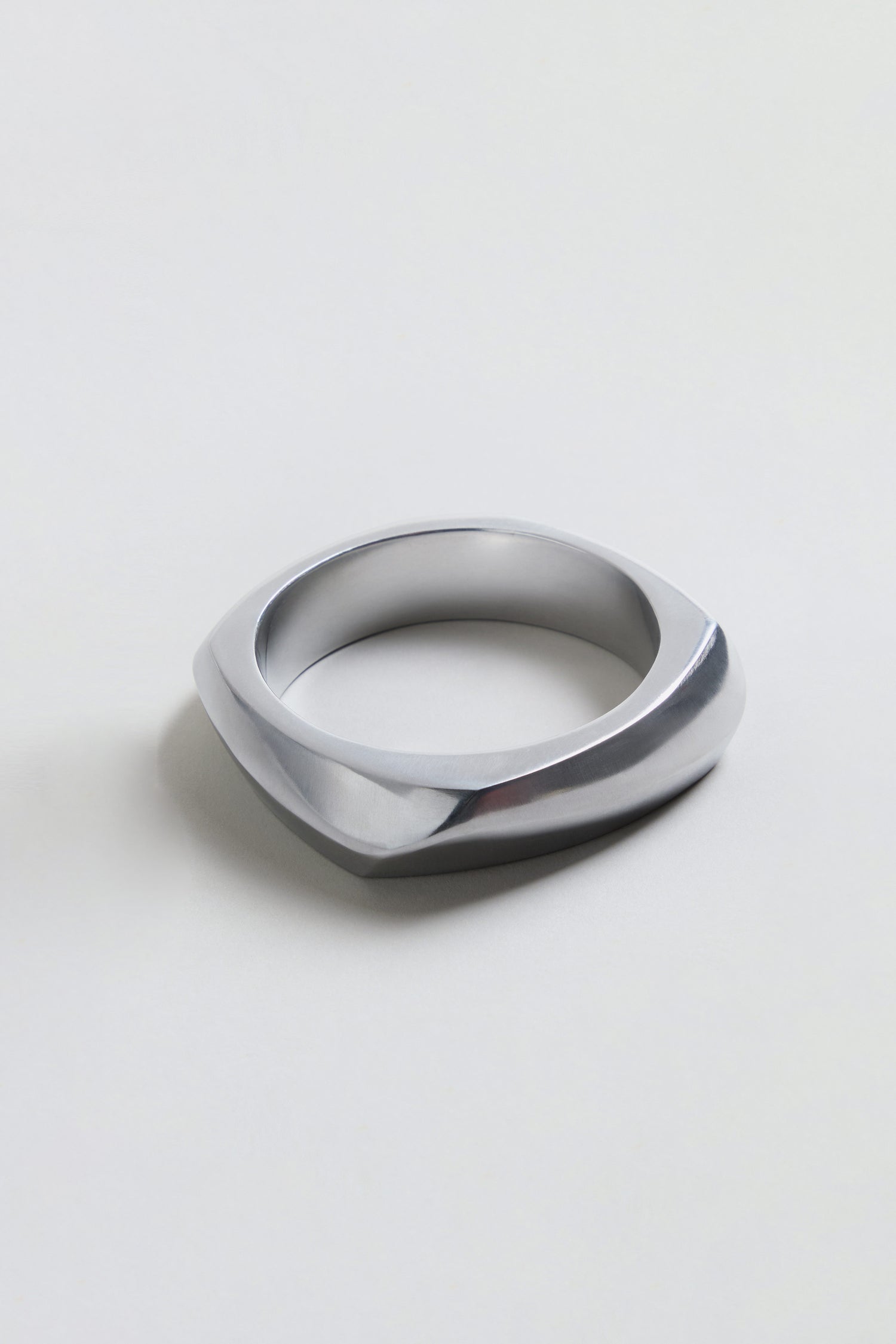 The Statement Silver Bangle, featuring a geometric and asymmetrical silver metallic design, rests on a plain light background and embodies the bold elegance of architectural jewelry.