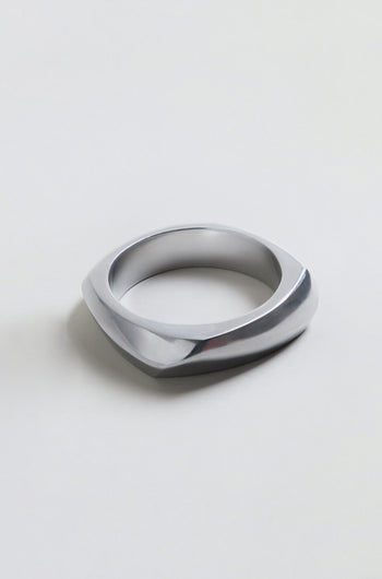 The Statement Silver Bangle, featuring a geometric and asymmetrical silver metallic design, rests on a plain light background and embodies the bold elegance of architectural jewelry.