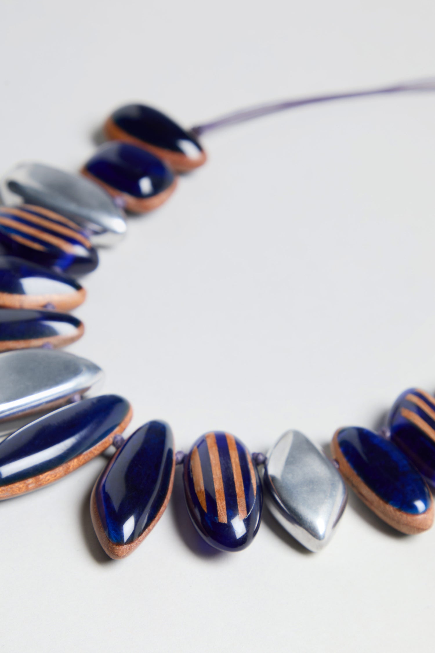 Here’s the revised sentence using your product data: A close-up of the Resin Pebble Necklace, showcasing dark blue oval beads with brown stripes and shiny silver accents, arranged in a partial circle on a light background. This striking design captures natural elegance and features an adjustable chain for the perfect fit.