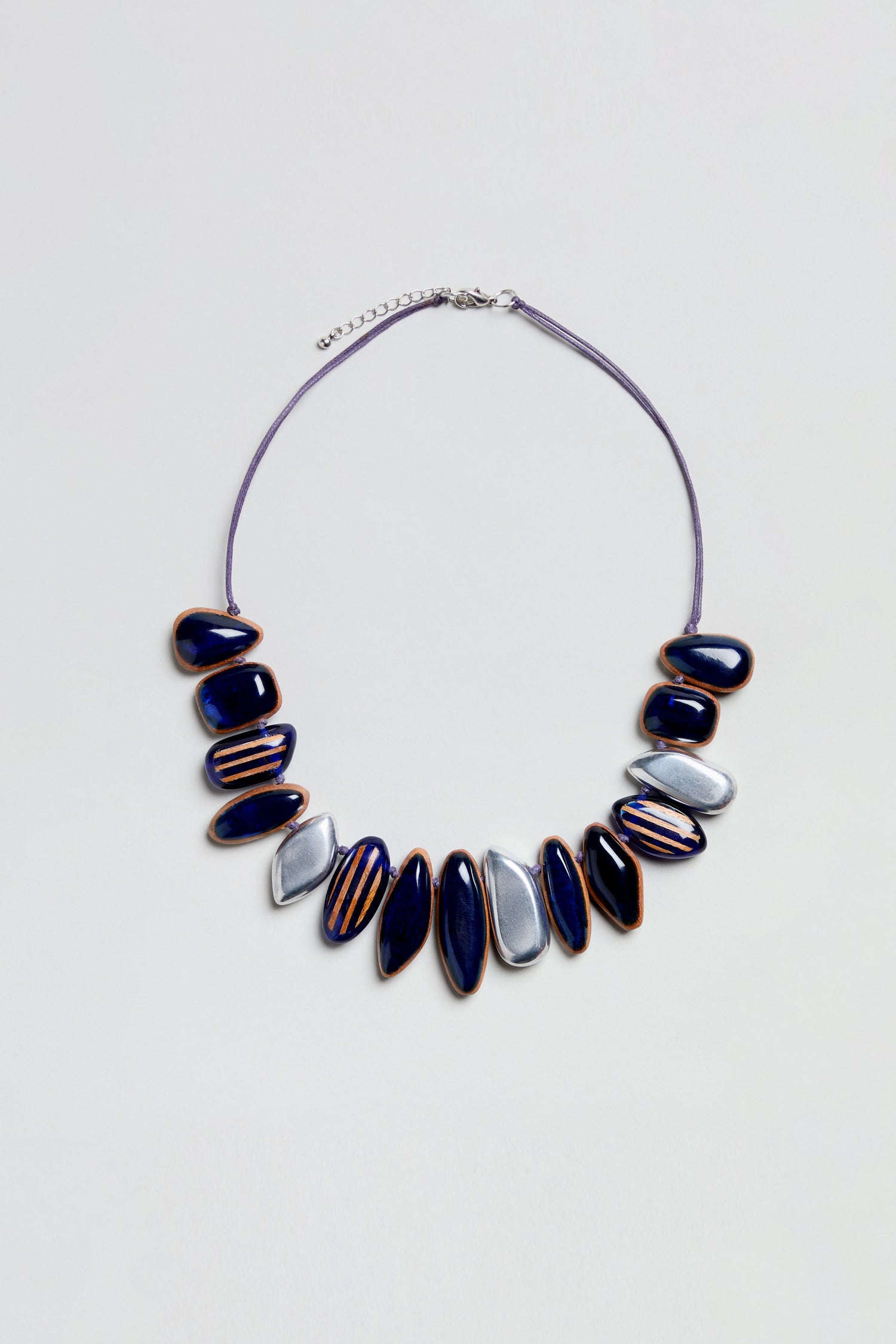 The Resin Pebble Necklace features alternating navy blue and silver oval beads—some adorned with gold detailing—arranged along a thin cord with an adjustable chain for the perfect fit, evoking the look of smooth resin pebbles.