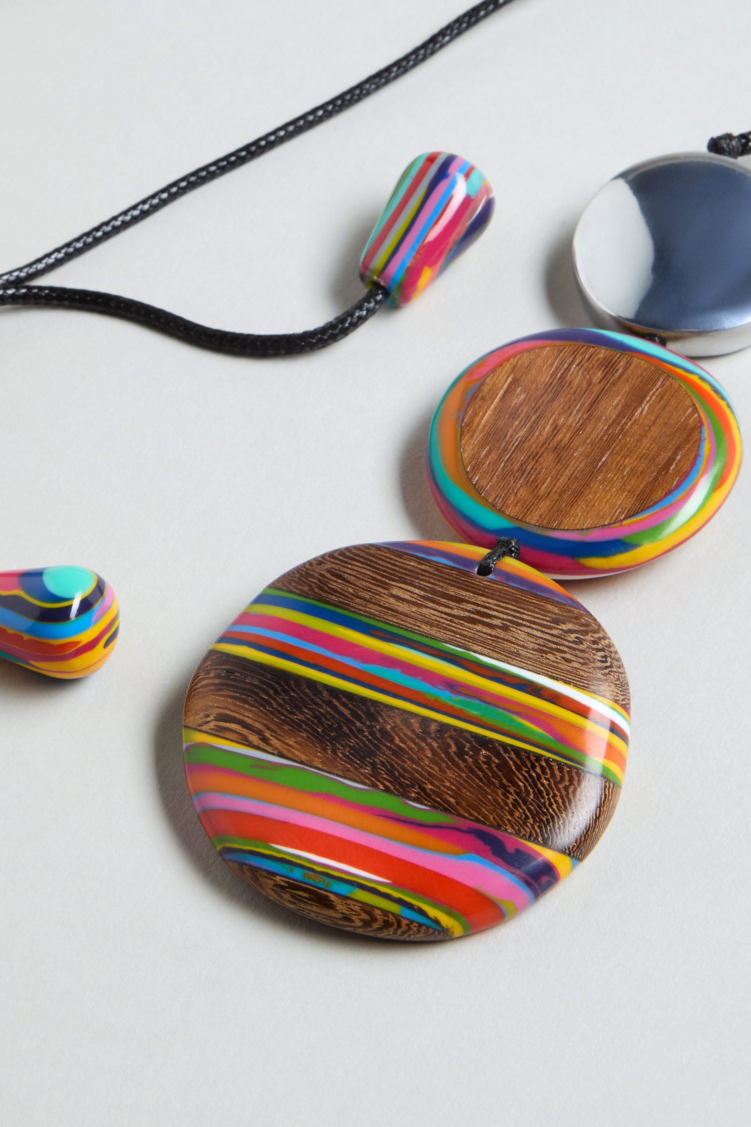 The Colourburst Triple Sphere Necklace is handmade jewellery featuring a multicolour resin design with a round wooden pendant, triple sphere accents, and matching earrings—beautifully displayed on a light background.