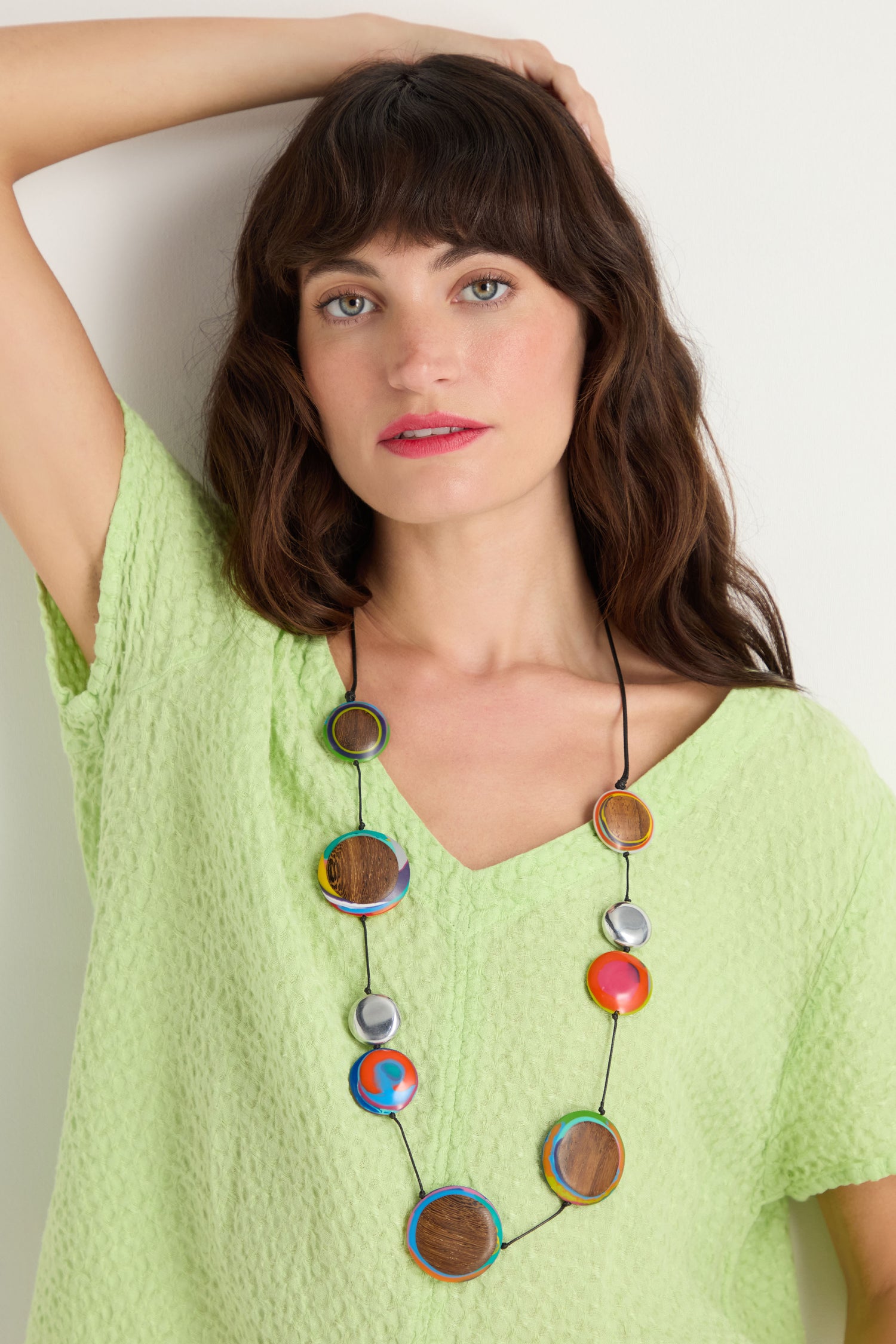 A woman in a light green textured top wears the Planetary Necklace, featuring large circular beads in wood, silver, red, and blue recycled aluminium, standing against a plain white background.