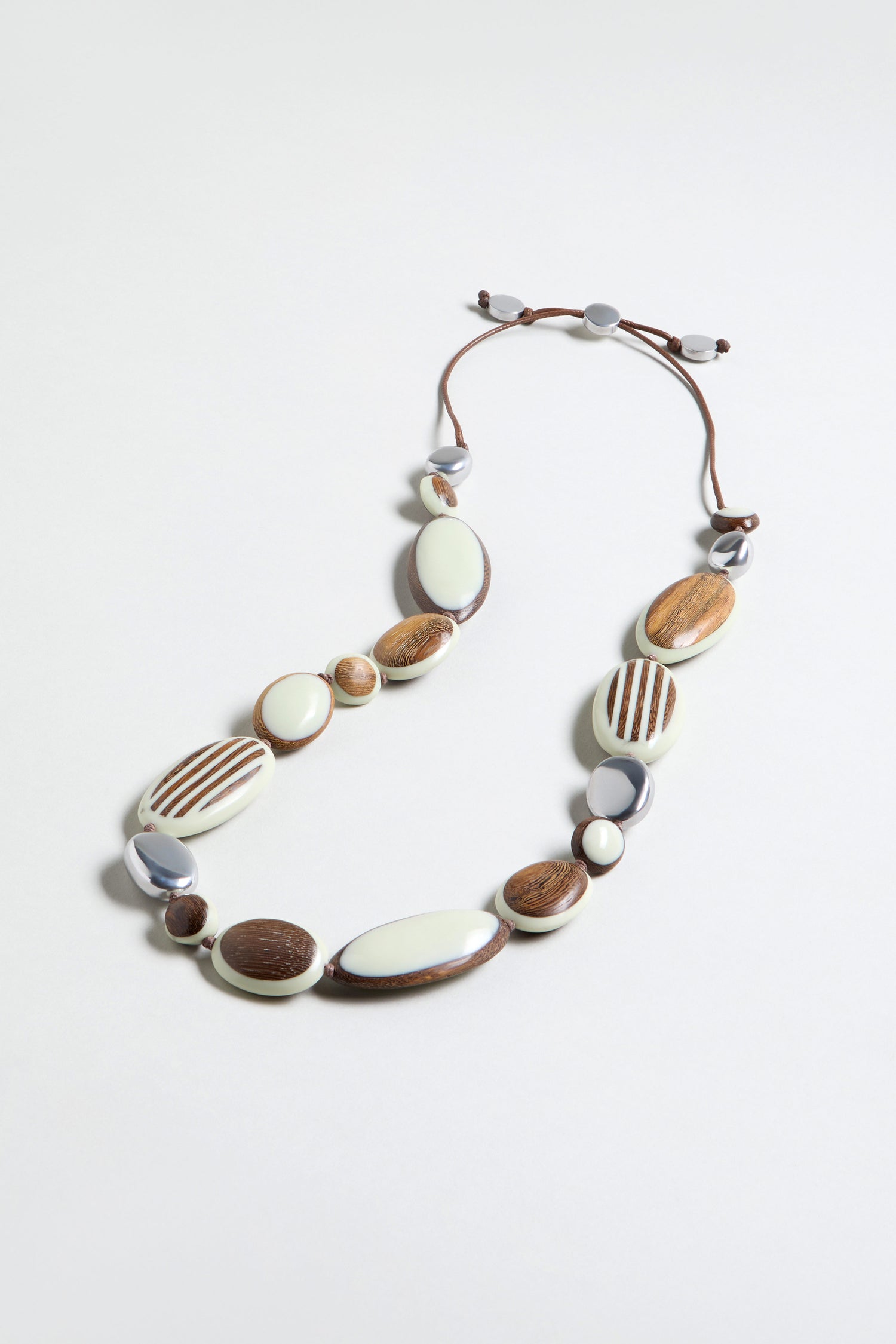 The Humbug Necklace showcases natural wood, white, and brown oval and round beads on a brown adjustable cord for an organic, earthy look.