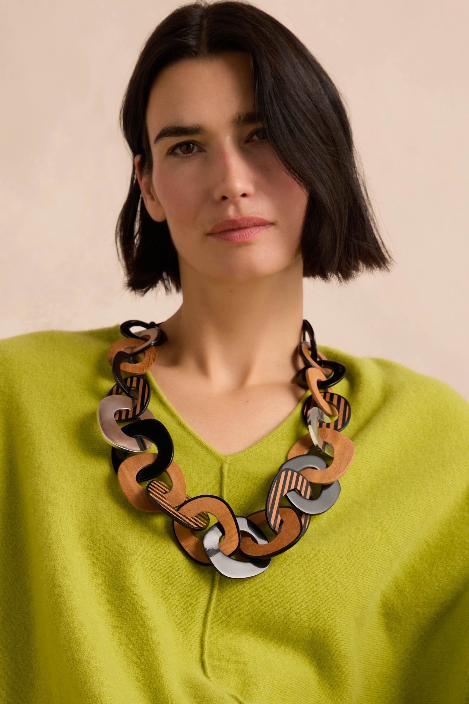 A woman with chin-length dark hair wears a lime green sweater and the Black Stripe Wooden Resin Links Necklace, looking at the camera against a plain light background.