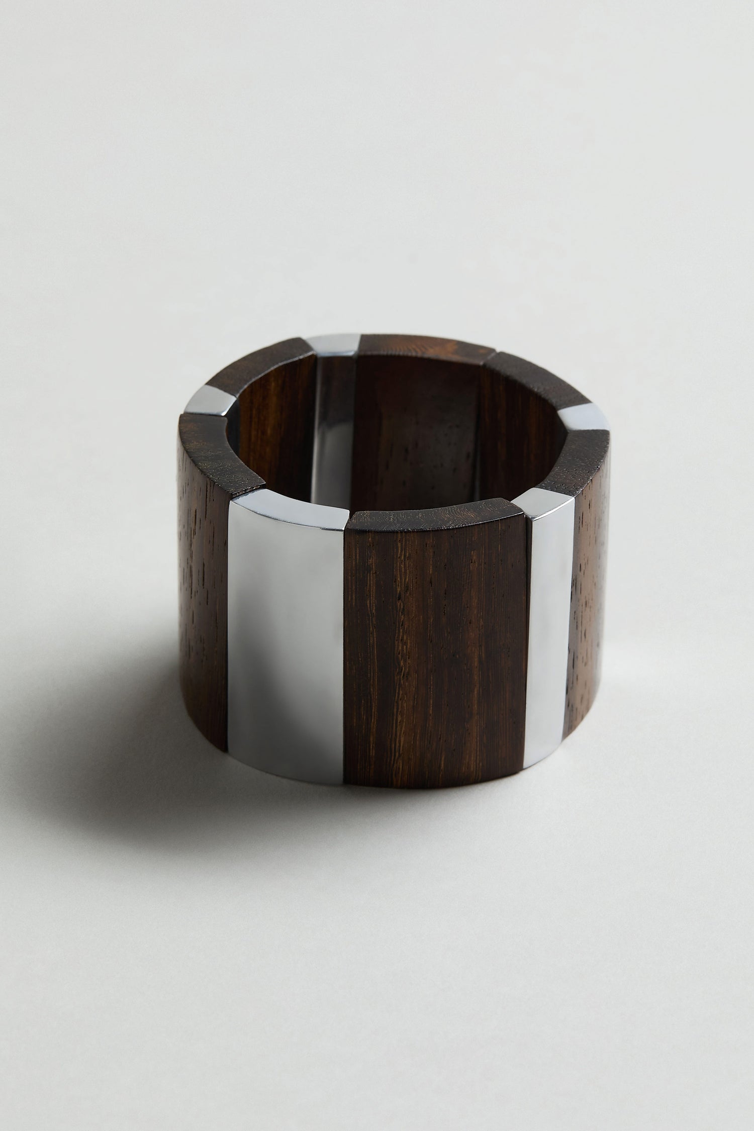 The Textured Wooden Bracelet showcases bold, wide silver metal inlays on rich dark wood. Handmade and photographed on a light background, this Ernesto de Barcelona design highlights its chunky, textured style.