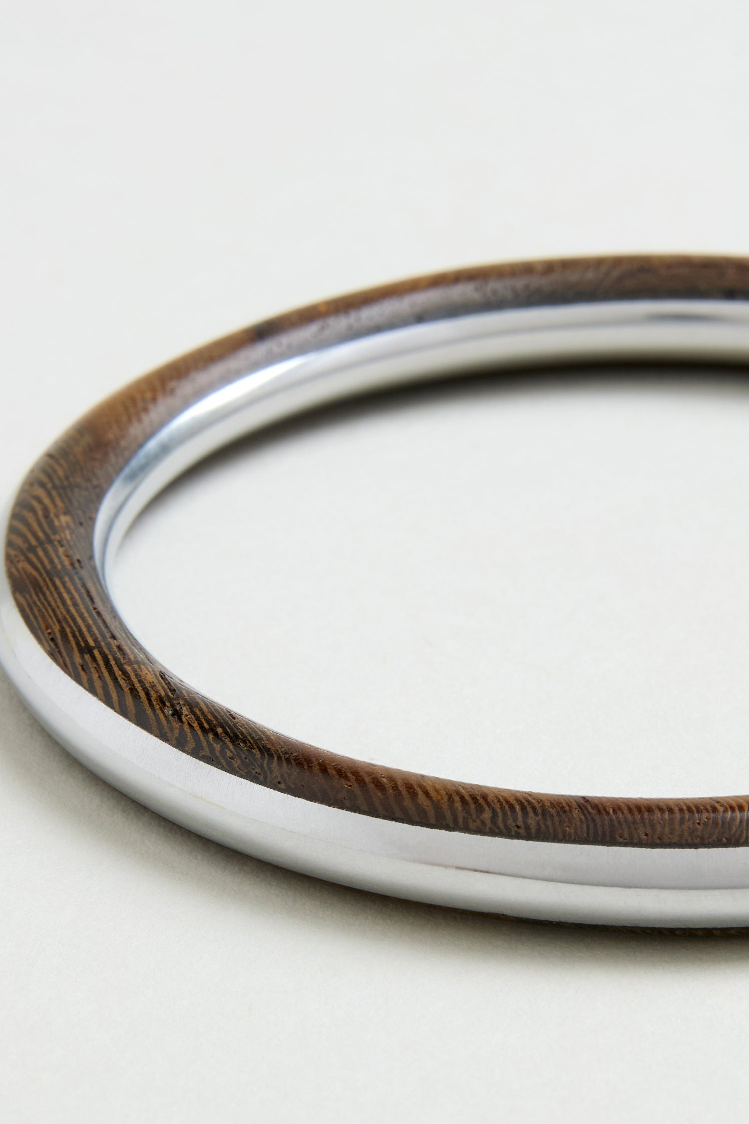 The Wooden Silver Fusion Bangle features a brown wooden exterior and a shiny silver interior, creating an elegant artisan jewellery piece perfect for any occasion.