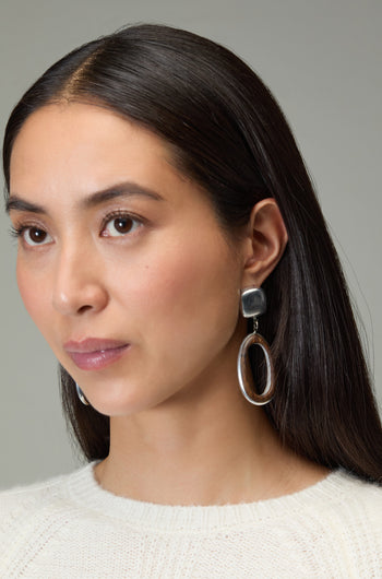 A woman with long dark hair wears a cream sweater and Wooden Silver Clip-On Earrings, looking slightly to the side against a plain background.