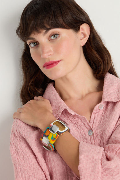A woman wearing a textured pink button-up shirt and the Colourburst Squares Link Bracelet poses with her hand on her shoulder, looking at the camera.