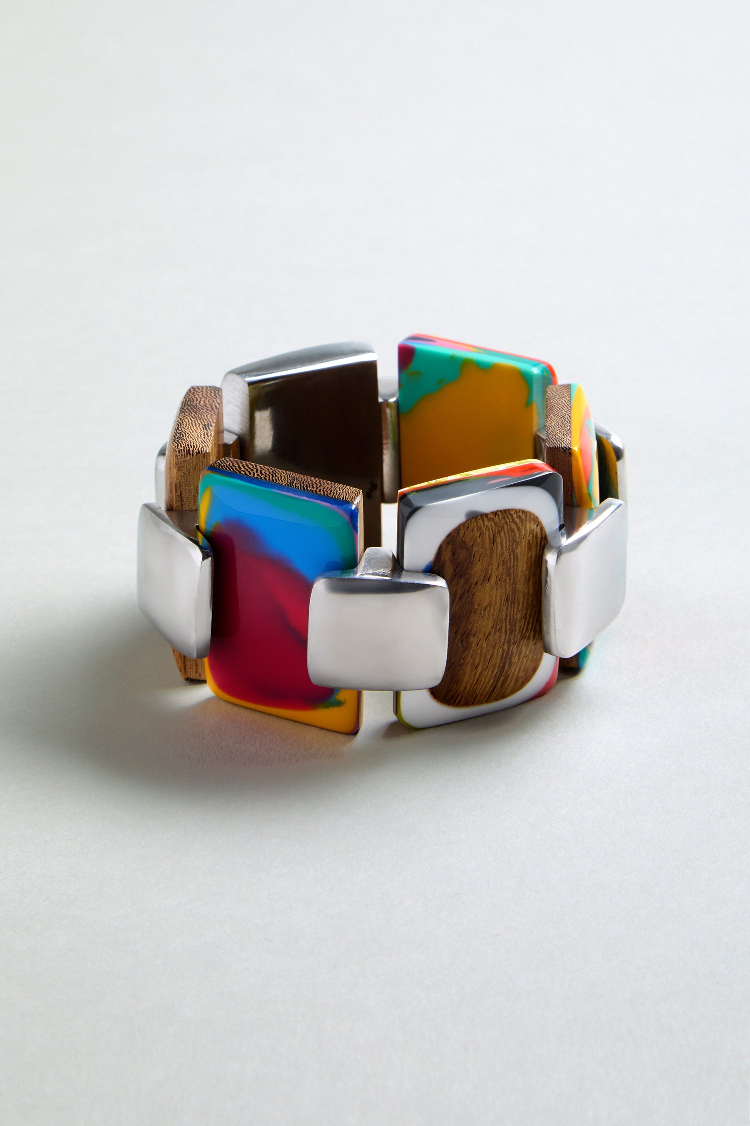 The Colourburst Squares Link Bracelet is a chunky multicolour resin piece with rectangular wooden, silver, and resin links in an alternating pattern, shown on a neutral surface.