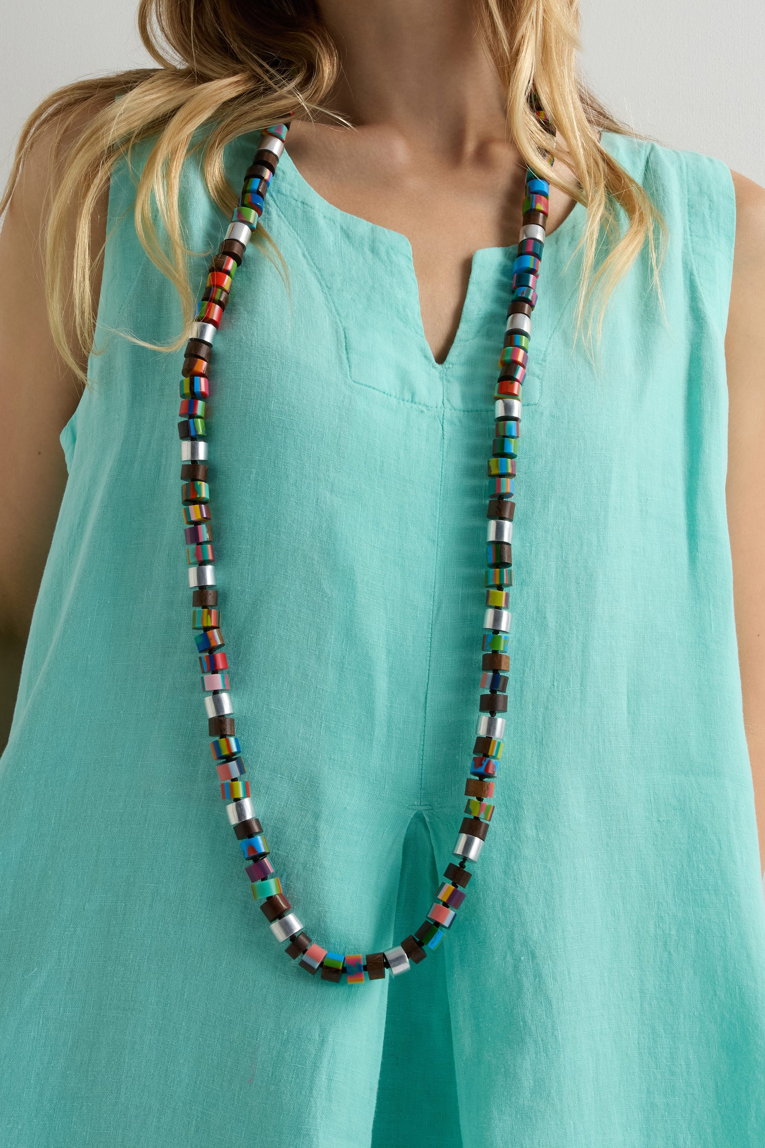 A person wearing a sleeveless turquoise top and the Venus Colourburst Cylinders Necklace.