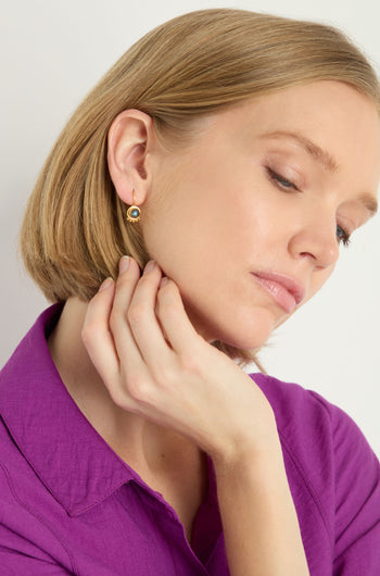 A woman with short blond hair, dressed in a purple collared shirt, touches her neck and looks downward while wearing Labradorite Stone Earrings.