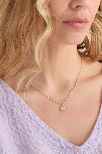A woman wears a textured light purple top and a Hand Crafted Moonstone Bead Necklace featuring a delicate round pendant.