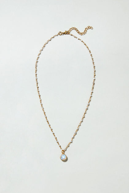 The Hand Crafted Moonstone Bead Necklace features gold plating, small beads, and a round translucent moonstone pendant, showcased against a simple light background.
