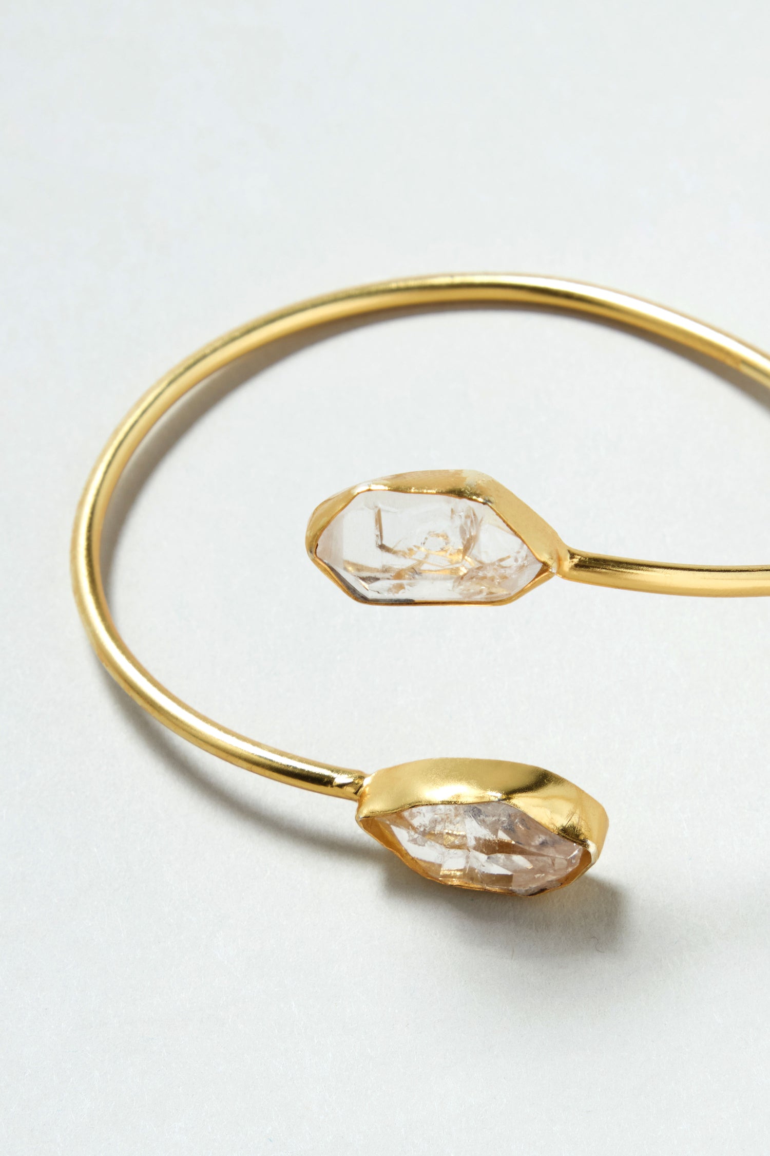 The Gold Plated Quartz Herkimer Diamond Bracelet is an 18k gold plated open cuff bangle with two irregular clear stones at each end, shown on a light background.