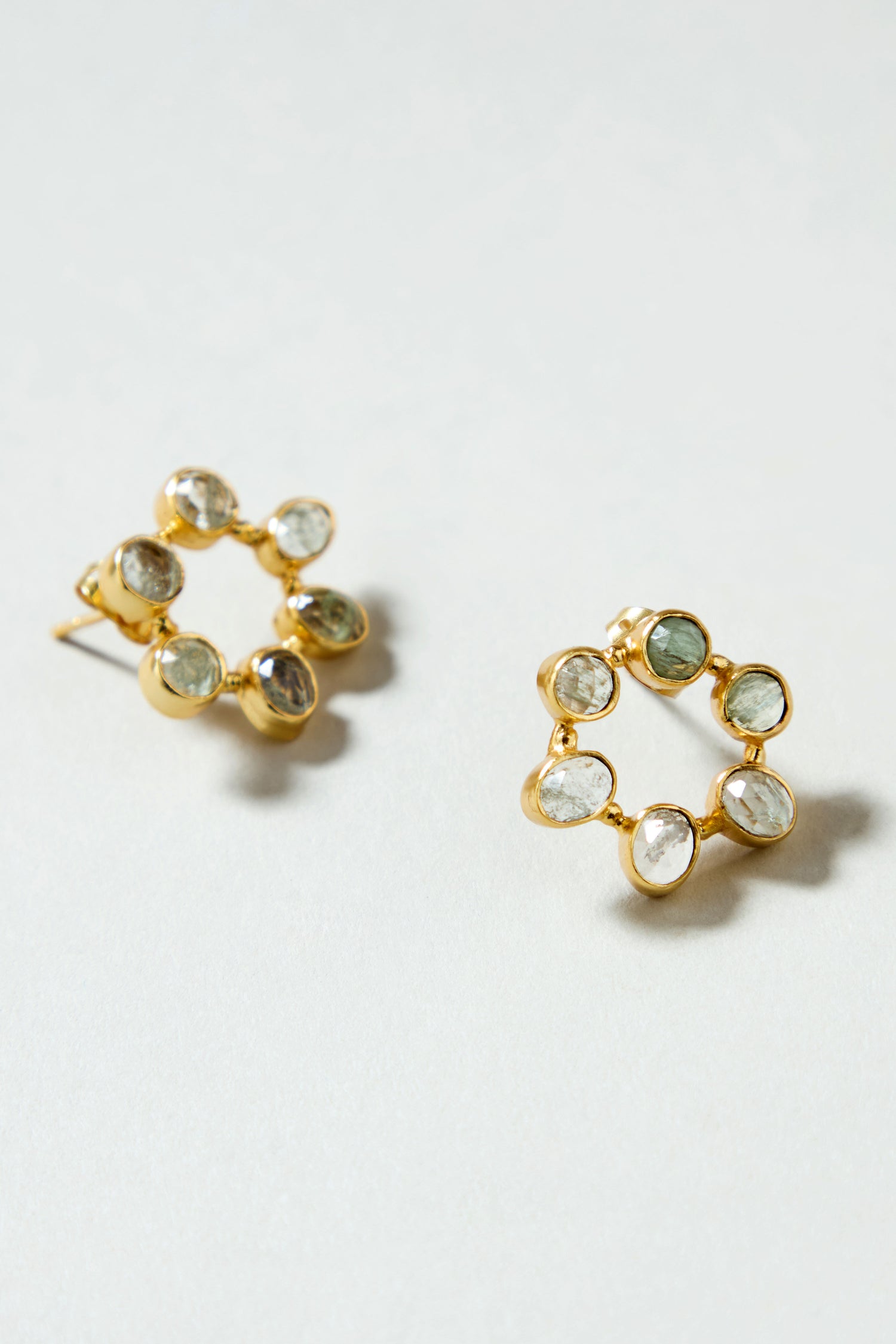 The Hand Crafted Aqua Crackle Mini Stone Earrings feature a gold-plated circular design with seven oval, transparent aqua gemstones around the edge, offering a unique handcrafted look.
