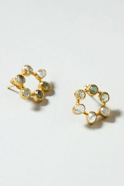 The Hand Crafted Aqua Crackle Mini Stone Earrings feature a gold-plated circular design with seven oval, transparent aqua gemstones around the edge, offering a unique handcrafted look.