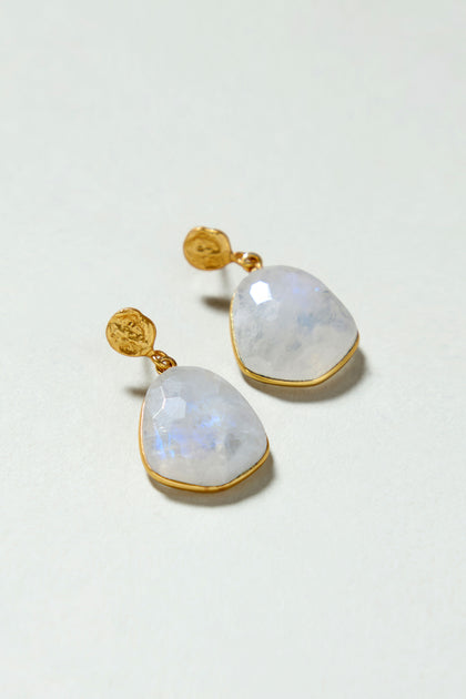 A pair of Hand Crafted Rainbow Moonstone Earrings featuring faceted, translucent white stones in irregular gold-plated drop settings, displayed on a neutral background.