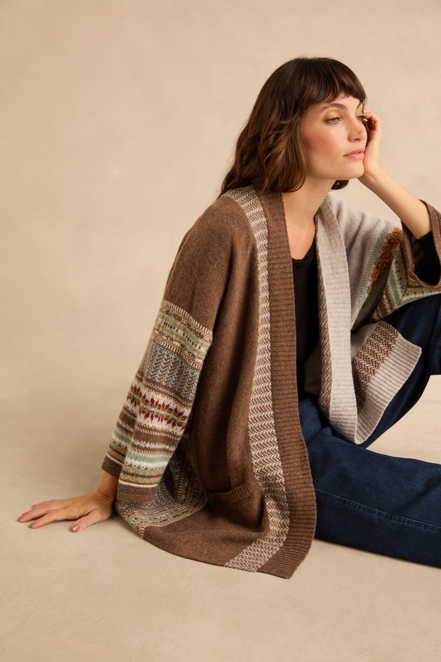 A person wearing a Mushroom Montrose Blanket Cardigan with a Fair Isle pattern, layered over a black top and dark jeans.