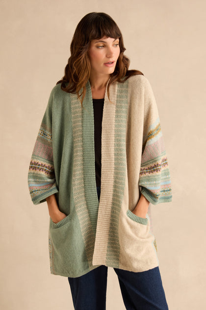 A woman wears an open Sage Montrose Blanket Cardigan in sage green and beige with a Scottish heritage Fair Isle knit pattern and pockets.