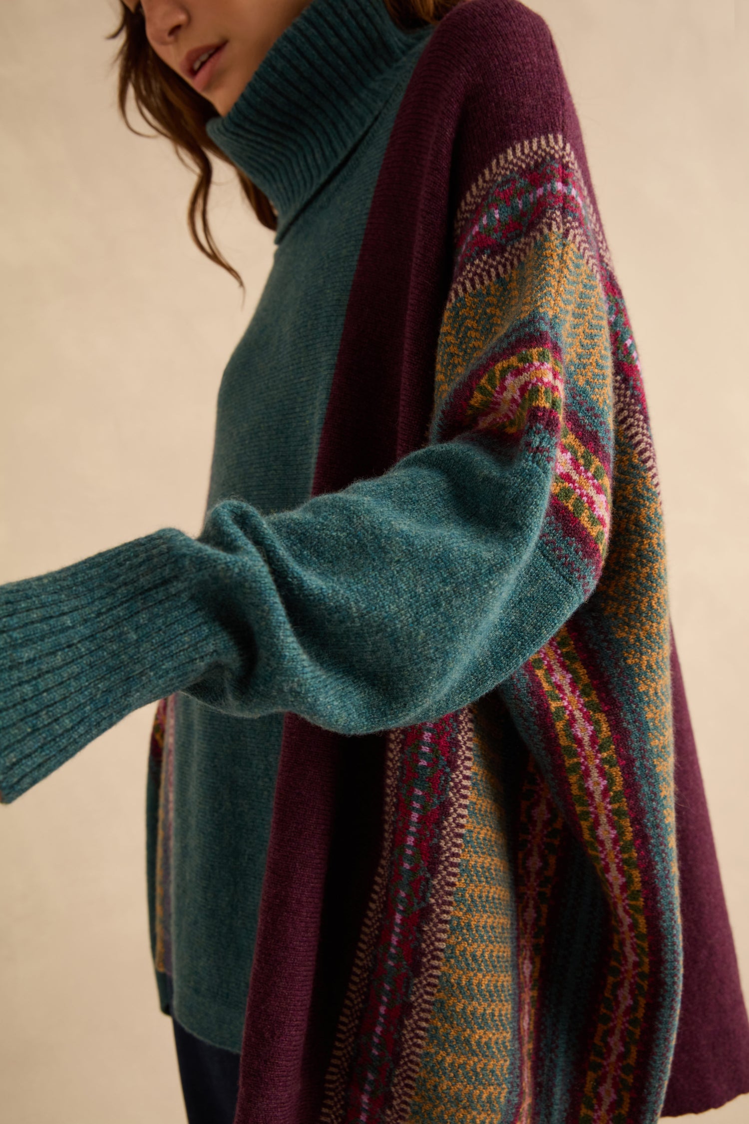 A person wearing a teal Hunter Montrose Cowl Neck Sweater layered under a plum-colored open cardigan featuring a Fair Isle patterned border.