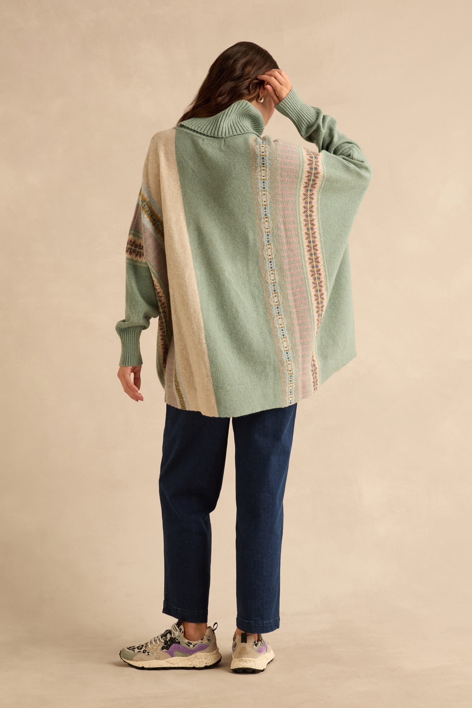 Back view of a person wearing an oversized sage green Sage Montrose Cowl Neck Sweater with vertical Fair Isle patterned stripes and dark blue jeans.