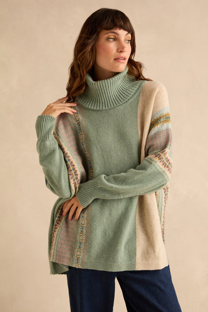 A woman wears a Sage Montrose Cowl Neck Sweater in sage green and beige, featuring an oversized fit, cowl neck, and patterned Fair Isle knit detailing on the sleeves and sides.