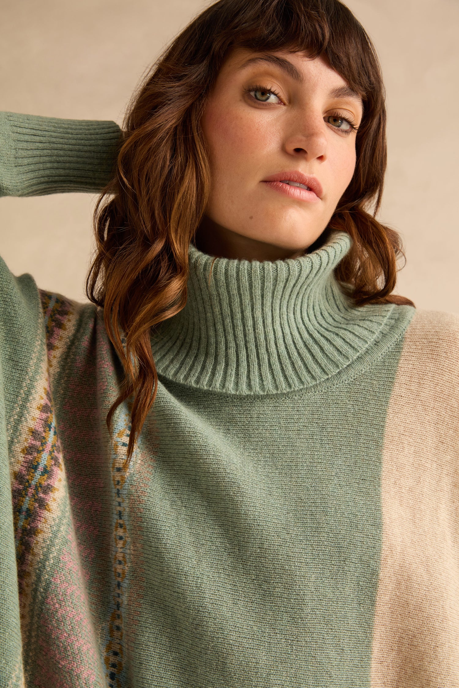A person wearing a Sage Montrose Cowl Neck Sweater in sage green merino lambswool with a subtle geometric Fair Isle pattern on the shoulder.