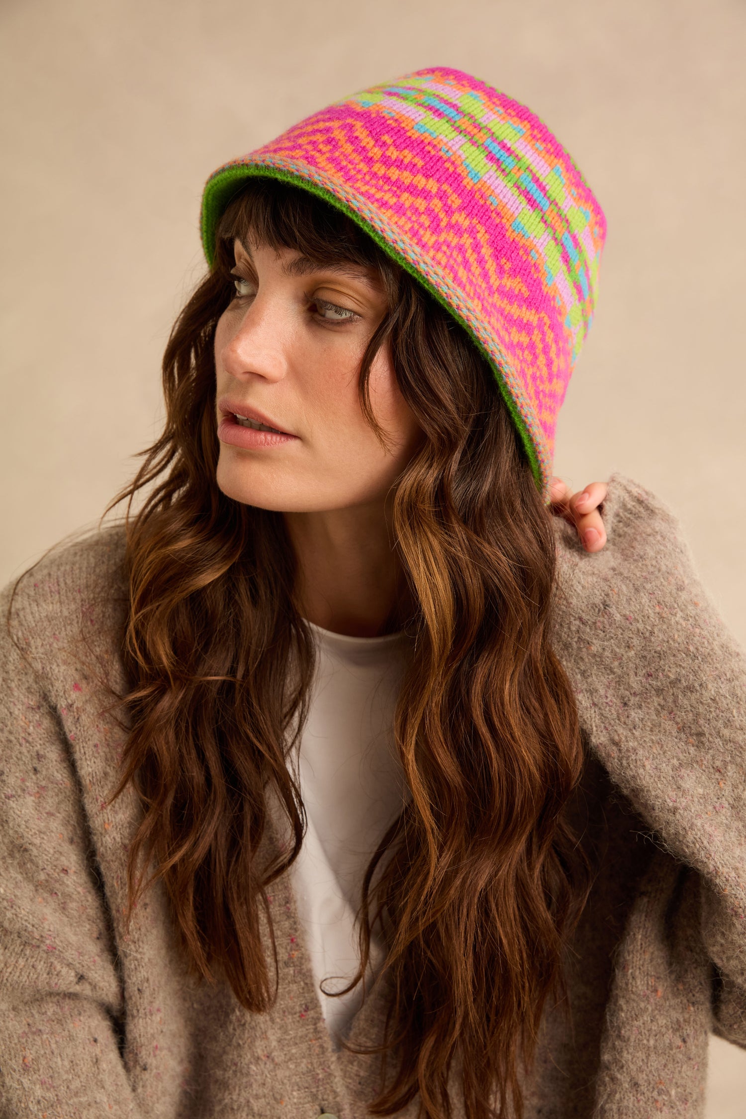 A person wearing a Stobo Graffiti Merino Bucket Hat in a multicoloured Fair Isle knit with a pink, orange, and green geometric pattern.