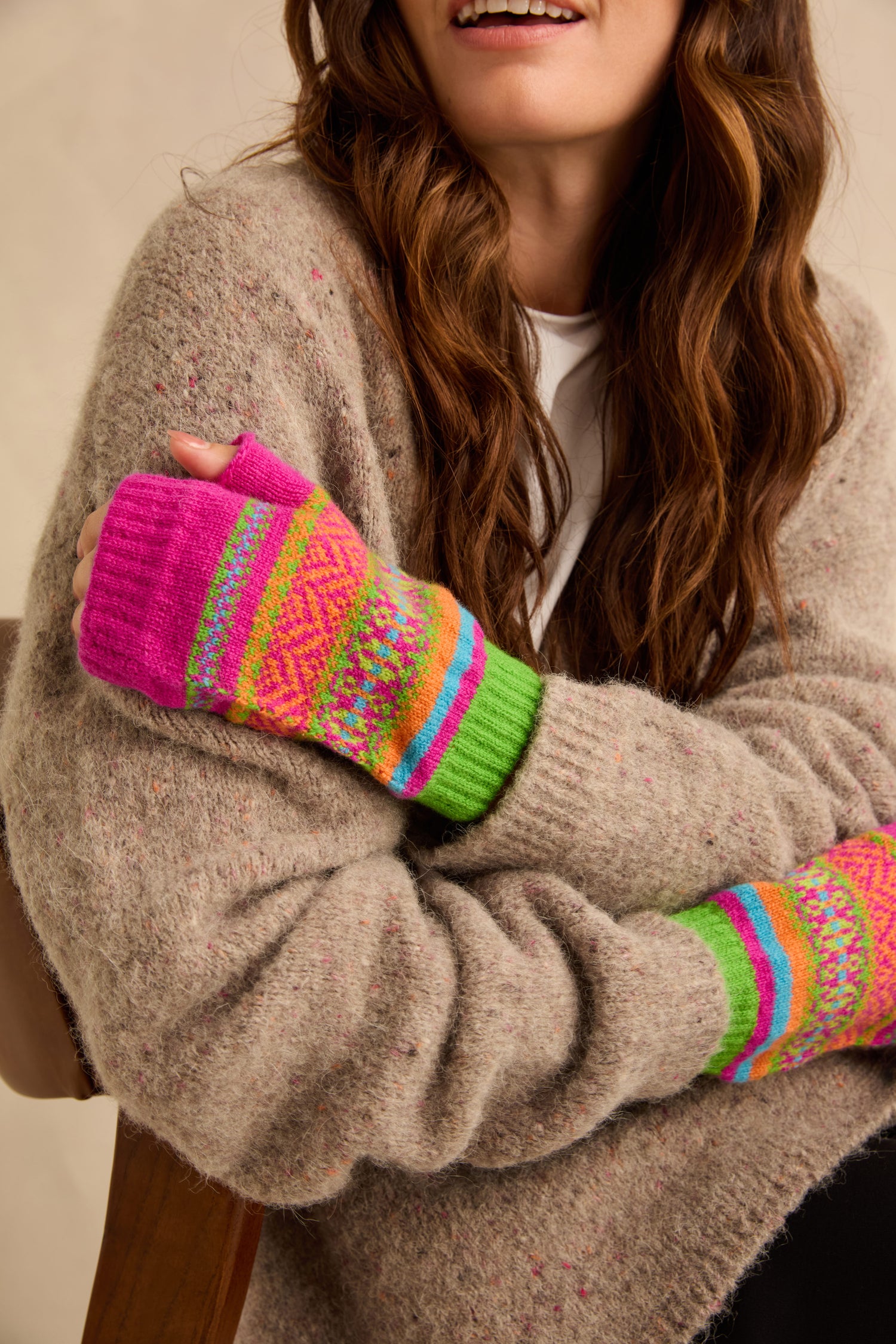 A person wearing Stobo Graffiti Merino Open Mitts, featuring a colorful geometric pattern with pink, orange, and green horizontal stripes.