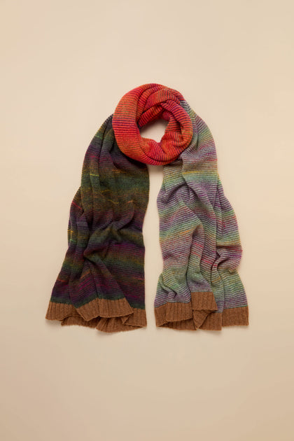 The Multicolour Treeline Merino Wool Scarf is knitted in Scotland, featuring a gradient of red, purple, and green horizontal stripes with solid brown ribbed ends.