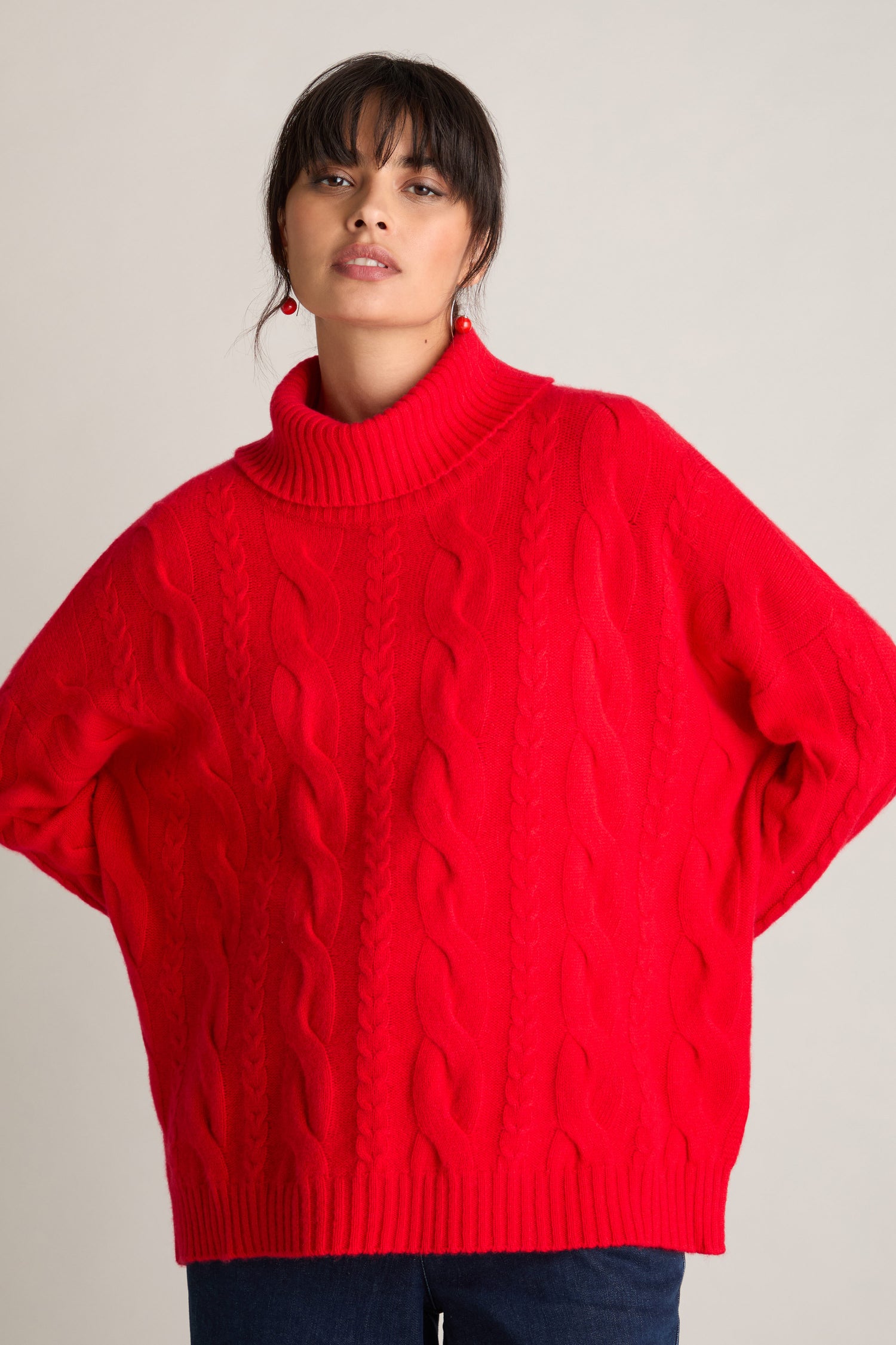 Person wearing a bright red Loose Cable Cashmere Knit with hands on hips, standing against a plain background.