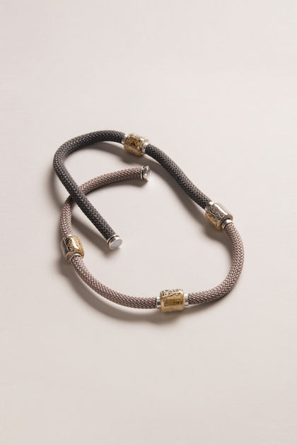 The Long Mosaic Bead Necklace features silver and gold cylindrical accents in a two-tone design inspired by Mediterranean jewelry, displayed on a neutral background.