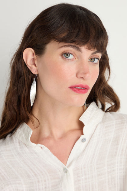 A woman with wavy brown hair wears a white textured blouse and Hammered Silver Leaf Earrings, looking at the camera against a plain background.