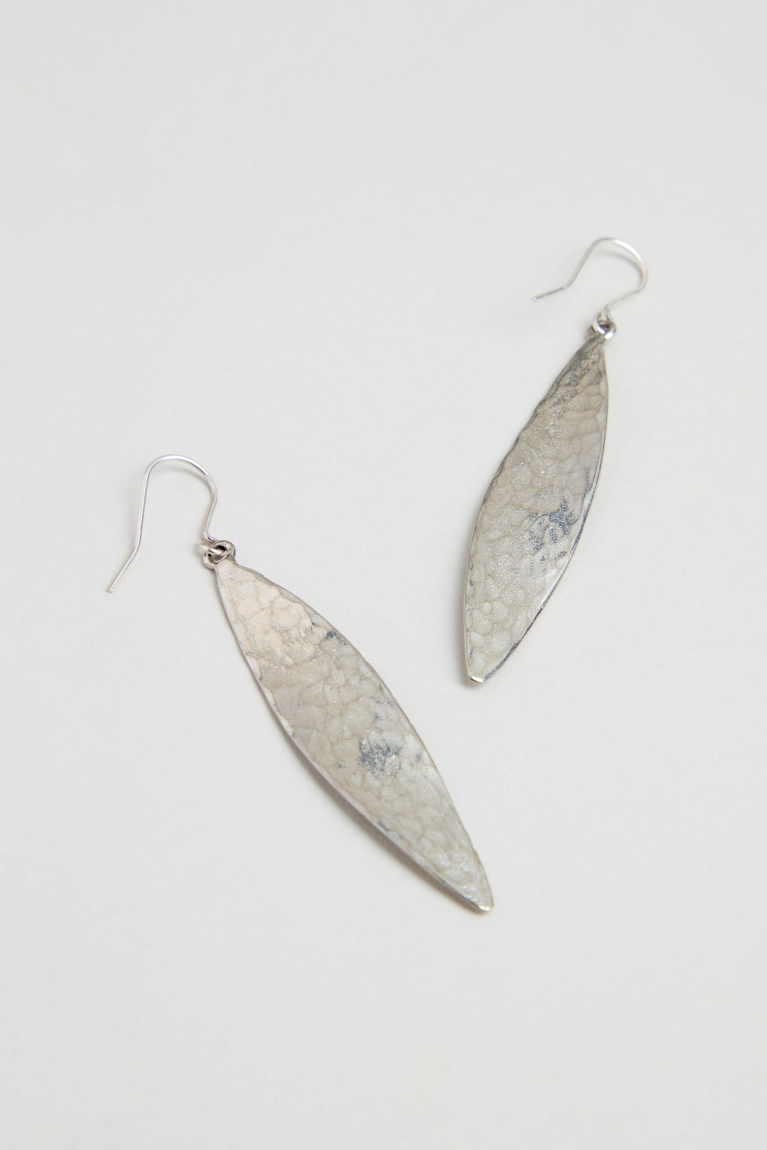 Hammered Silver Leaf Earrings with a textured finish dangle elegantly in a leaf-shaped design against a plain white background.
