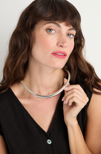 A woman with long brown hair and light eyes wears a black top and holds the Grey Leather Cord Necklace near her neck, looking directly at the camera.
