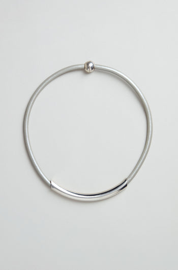 The Grey Leather Cord Necklace is a simple, minimalist piece featuring a curved metal bar and round clasp, presented on a plain light background.