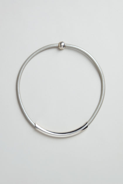 The Grey Leather Cord Necklace is a simple, minimalist piece featuring a curved metal bar and round clasp, presented on a plain light background.