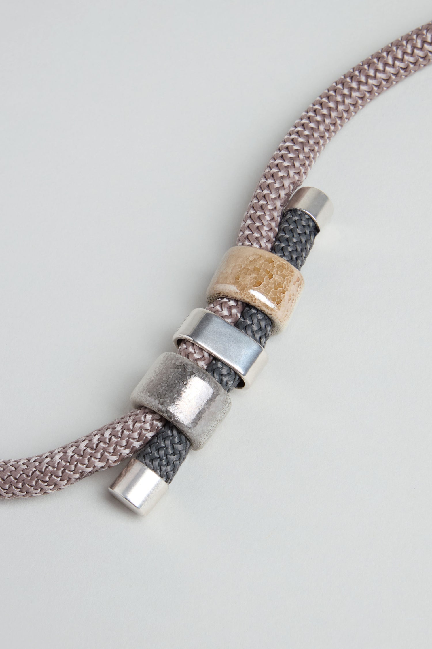 A detailed view of the Layered Marble Bead Cord Necklace showcases its braided cord and layered design, featuring metallic silver and beige marble-effect beads against a light background.