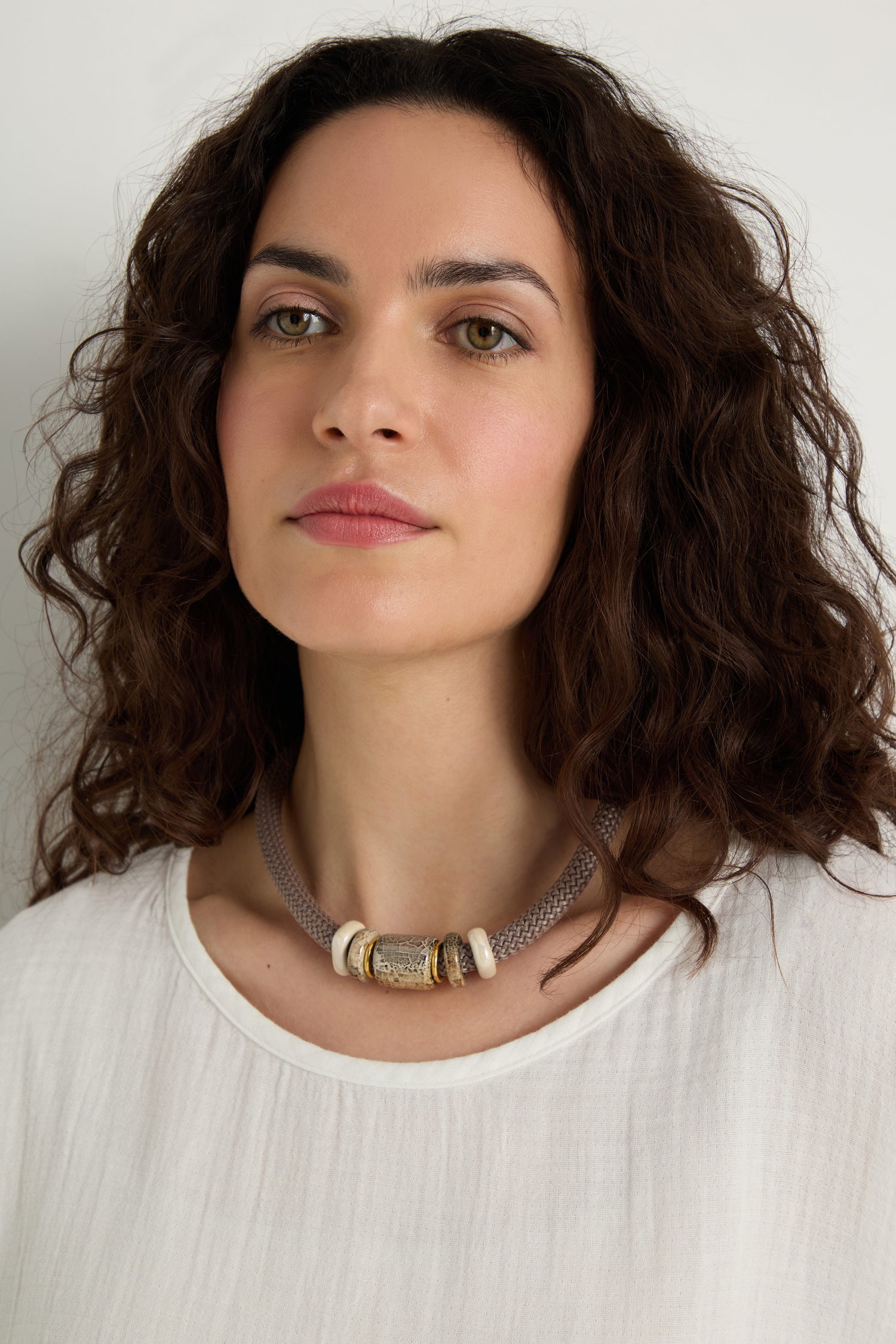 Woman with wavy dark hair wearing a white blouse and a Mosaic Marble Bead Short Cord Necklace, posed against a plain light background.