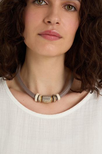 A woman with wavy brown hair wears a white top and the Mosaic Marble Bead Short Cord Necklace, featuring a large decorative central bead and white accents.