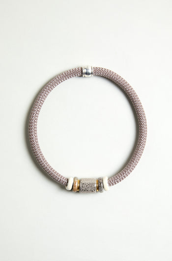 The Mosaic Marble Bead Short Cord Necklace features a woven light mauve cord, a cylindrical silver centerpiece, and two white and gold accent rings, elegantly displayed on a plain light background.