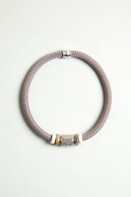 The Mosaic Marble Bead Short Cord Necklace features a woven light mauve cord, a cylindrical silver centerpiece, and two white and gold accent rings, elegantly displayed on a plain light background.