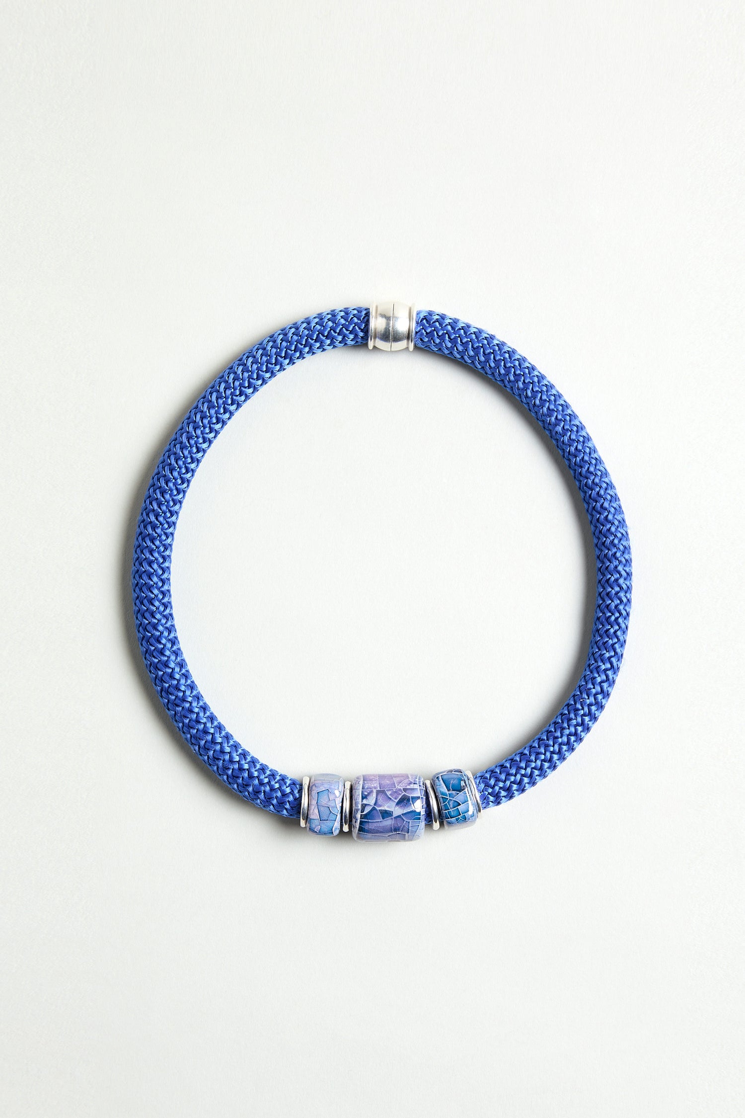The Triple Marble Bead Short Cord Necklace features three patterned blue and silver cylindrical beads, silver accents, and a chunky cord design, beautifully displayed on a light background.