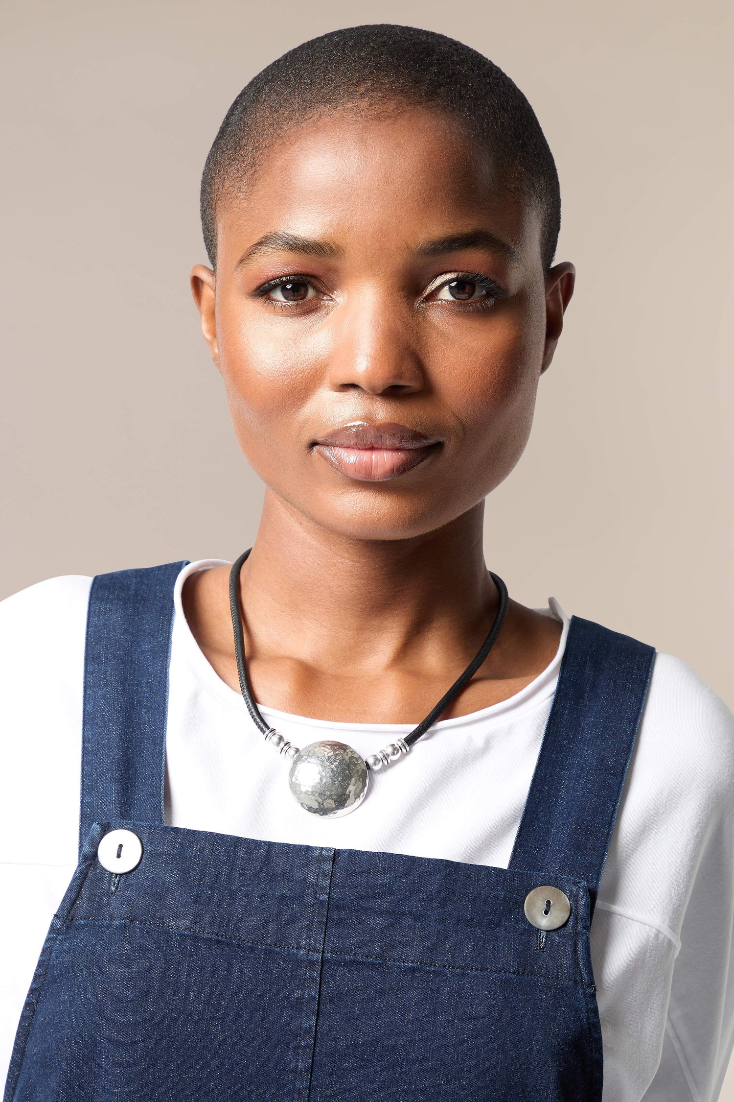 A black woman wearing overalls and a Mini Hammered Sphere Necklace.