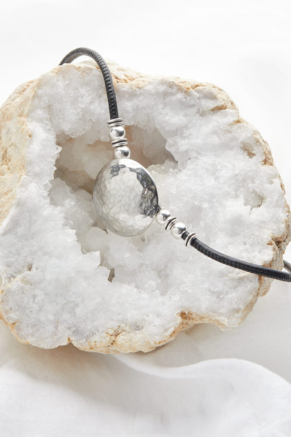 A Mini Hammered Sphere Necklace sits on top of a white rock, resembling a stunning necklace.