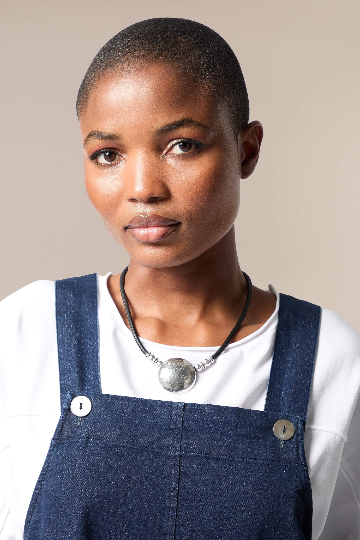 A black woman wearing overalls and a Mini Hammered Sphere Necklace.