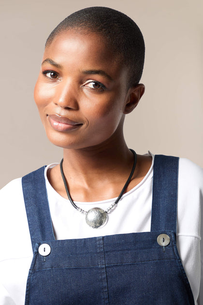 A black woman wearing overalls and a Mini Hammered Sphere Necklace.