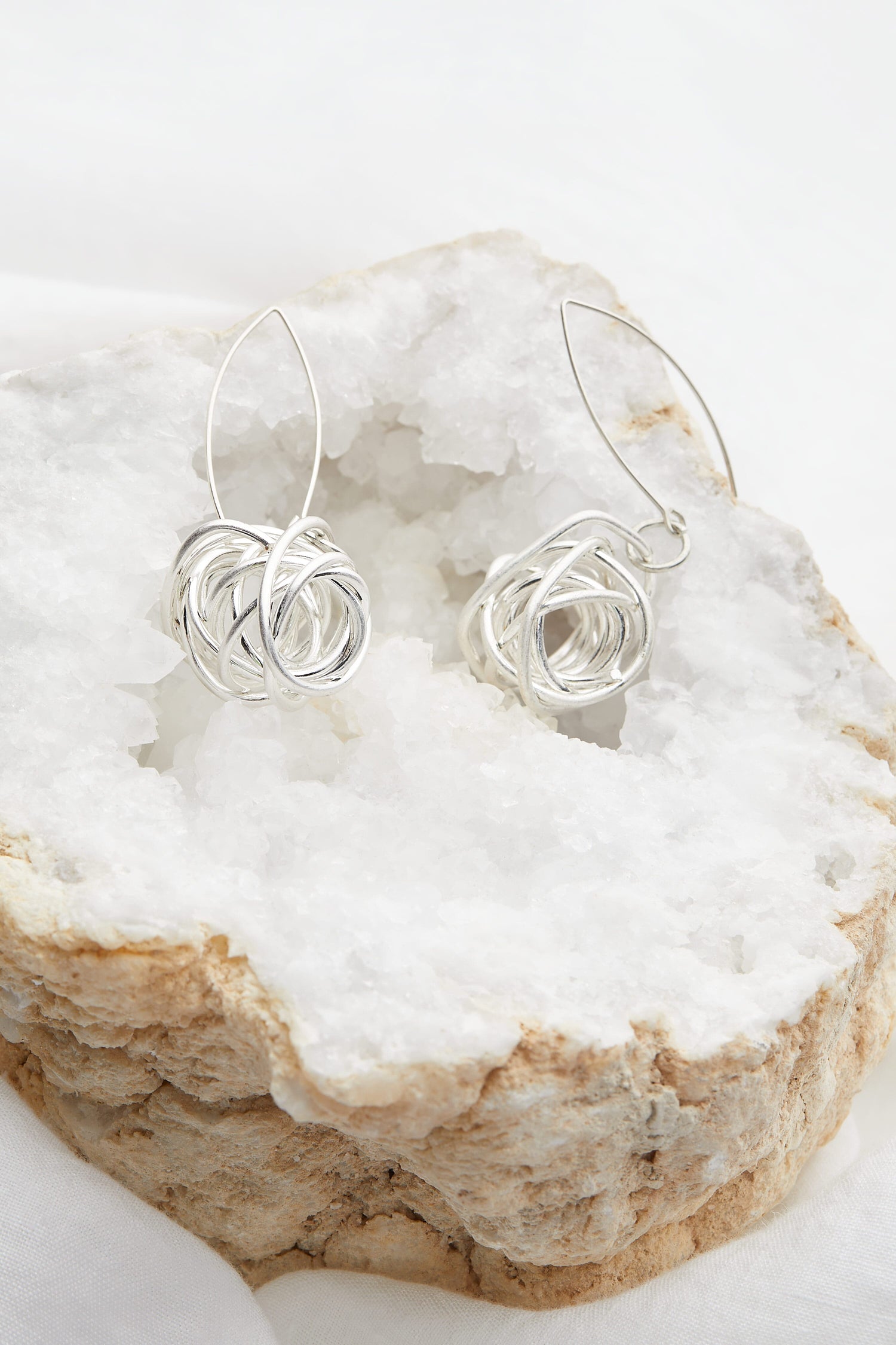 A pair of Silver Squiggle Earrings sitting on a rock, beautifully adorned with beads.