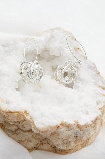 A pair of Silver Squiggle Earrings sitting on a rock, beautifully adorned with beads.